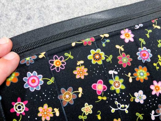 A hand holds a black zipper that has just been sewn to a piece of black floral fabric. This sits on top of a grey pressing mat.