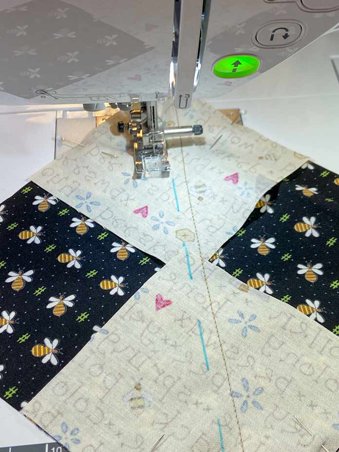 A close-up of the J foot on the Brother NQ900 sewing machine. One side of the foot is lined up with the blue diagonal line on the back of the yellow fabric. A line was already sewn down the opposite side of the drawn line.