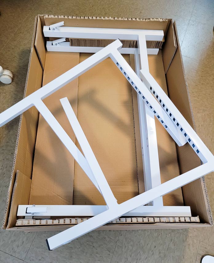 Four pieces of white metal for table legs in an open brown box