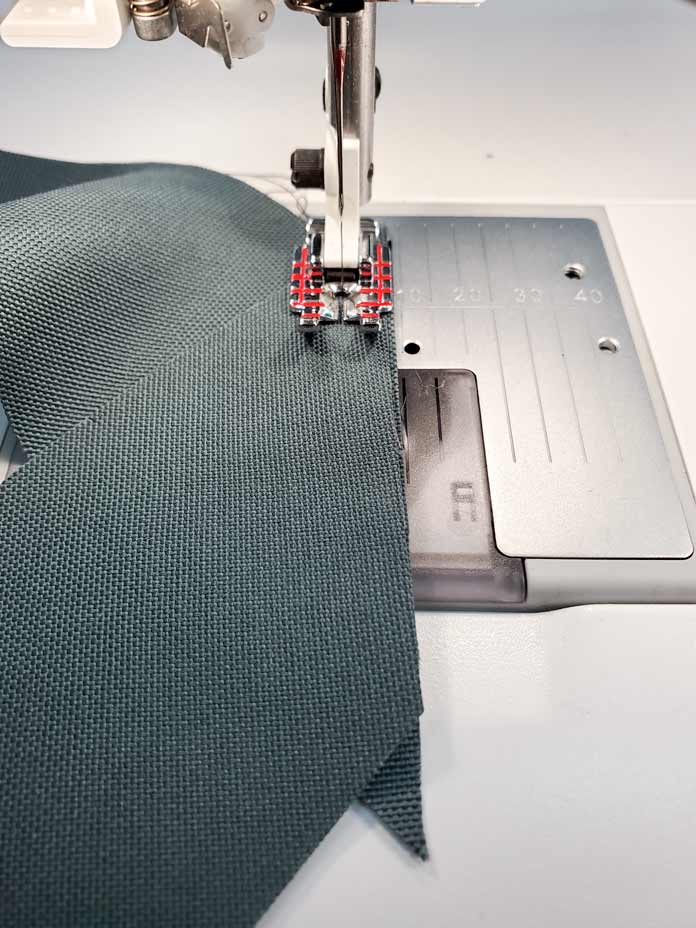 Two bias strips of green fabric are under the metal foot of a sewing machine
