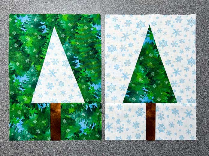 2 tree quilt blocks next to each other on a gray background. The first block has a white snowflake tree with a brown tree trunk and green background. The second block has a green tree with a brown tree trunk and white snowflake background