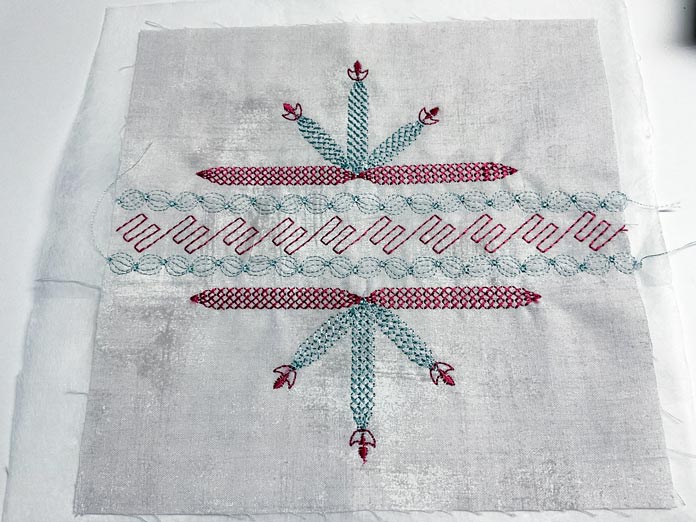 A piece of beige fabric used as a decorative stitch sample showing tapering stitches in red and green thread 
