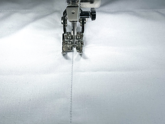 Two stitch lines are sewn down the center of a piece of white fabric
