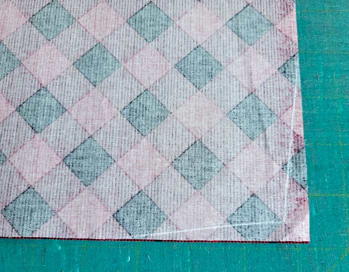 The wrong side of a red and black plaid fabric with two angled chalk lines