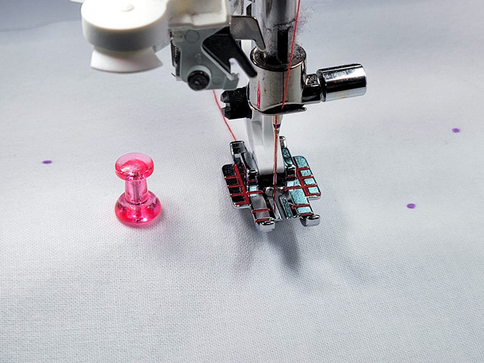 A pink push pin beside a sewing machine presser foot on white fabric; Husqvarna Viking Designer EPIC 2