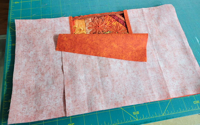 Three pieces of orange fabric on a green cutting mat