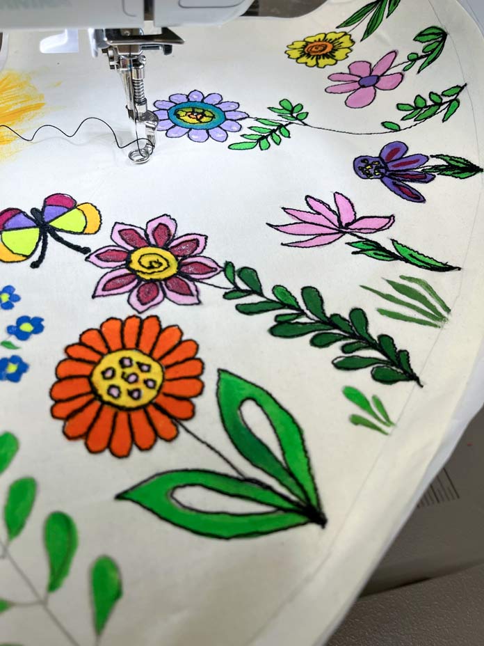 Painted flowers in oranges and pinks and purples are outlined with black stitching on white fabric; Gütermann Thread, Fabric Creations 100% Cotton Fabric