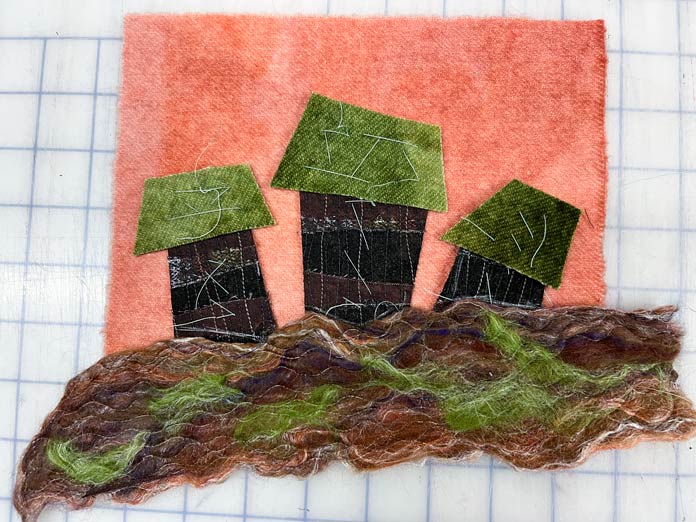 Brown and green stitched wool roving and brown cotton fabric houses with green wool roofs are ready to appliqué to and orange wool background; Solvy Water Soluble Stabilizers