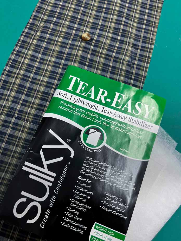A package of Sulky Tear–Easy stabilizer laying on shirt fabric; OMNIGRIP Ruler 8½" x 8½", OLFA 45 mm Ergonomic Rotary Cutter, OLFA Endurance Rotary Blades, Sulky Tear-Easy stabilizer, Odif 505 Adhesive Fabric Spray, OLISO PRO TG1600 Pro Plus Smart Iron, Mary Ellen’s Best Press, Best Press Spray and Misting Bottle