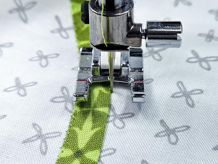 A green strip of fabric on a white background with a metal presser foot