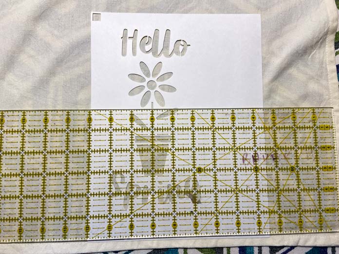 A yellow rotary cutting ruler is shown sitting on top of a freezer paper stencil which is on a beige tea towel; Sew Easy Freezer Paper for Quilting and Applique, Omnigrid ruler - 6" x 24"