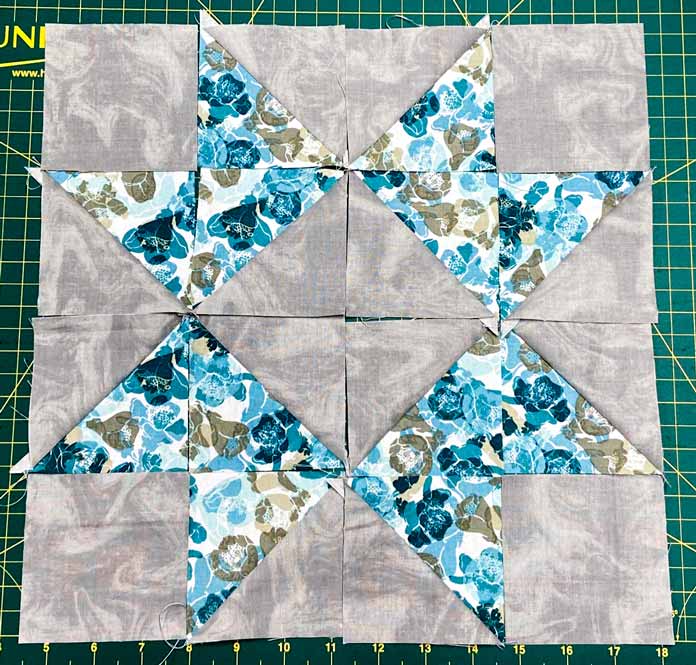 A star quilt block made with blue floral and gray HST units and gray squares on a green cutting mat. Omnigrid Triangle Ruler for Half Square Triangles, Fabric Creations 100% Cotton Fabric, Fairfield Crafter’s Choice Pillow Form, SCHMETZ Microtex Needles, Gütermann Cotton 50wt Thread, clover Ball Point Awl, UNIQUE Wool Pressing Mat