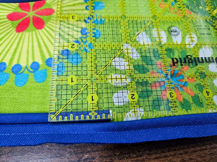 Blue piping on green fabric with a quilter’s ruler; Gütermann Nostalgia Box - 50wt Cotton Thread 100m - 48 Shades, Gütermann Nostalgia Box, Flat Felled Foot 9mm, Husqvarna VIKING Opal 690Q, free sewing pattern, outdoor accessories, outdoor cushions, piping, Husqvarna VIKING 8” Bent Trimmer