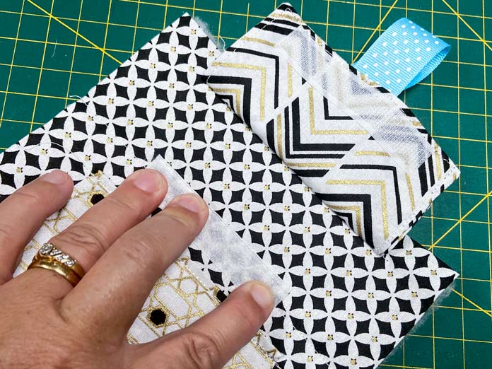 A hand presses down on a short hook and loop tape on a black and white fabric. A green cutting mat can be seen in the background.