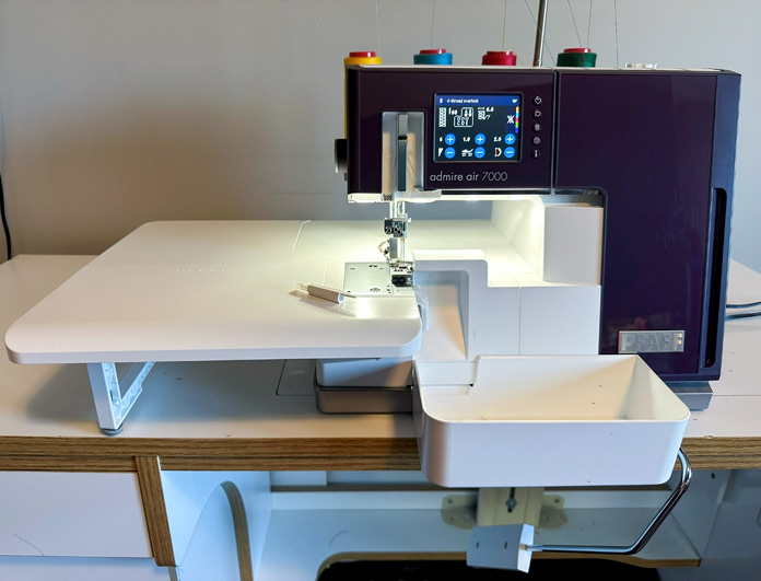 A purple and white serger, with extension table, setup ready to stitch, with waste tray and knee-lifter installed; PFAFF admire air 7000