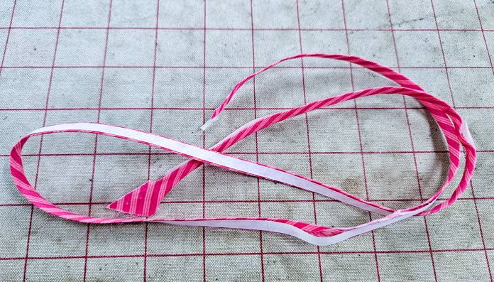 A strip of pink fabric with white tape; HeatnBond Lite, fusible bias, Clover bias tape maker, sewing supplies. 