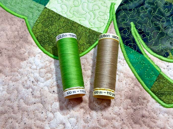 a green and cream colored 100m spools of Gütermann thread place on top of the clover quilt.