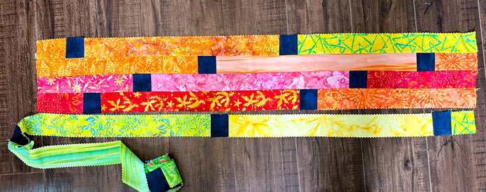 4 rows of the vibrant jelly roll strips and navy mottled squares, trying to plan which side and which way is “up” so that the navy squares do not touch 