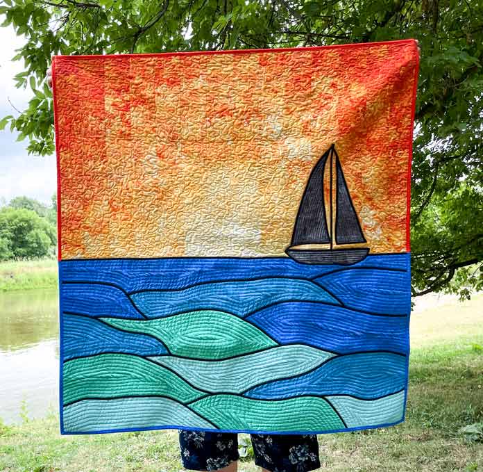 A quilt of a sailboat on water entitled Come Sail Away Quilt.