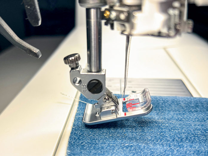 A detailed close-up image of the PFAFF Creative Icon 2’s needle area, showing the PFAFF 2A Fancy Stitch Foot attached. The machine is stitching on denim fabric. The presser foot is specialized for ribbon embroidery and decorative techniques and does not engage the IDT system. The red lines on the transparent foot help guide stitch placement, and the needle is centered over the fabric, ready for a decorative ribbon stitch.