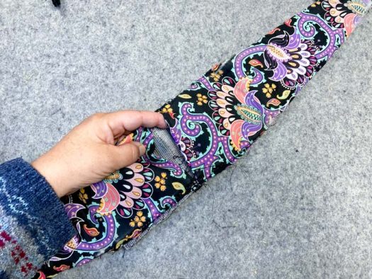 A hand holds a multicolored section of a purse and shows the vinyl piece that is inside the middle. 