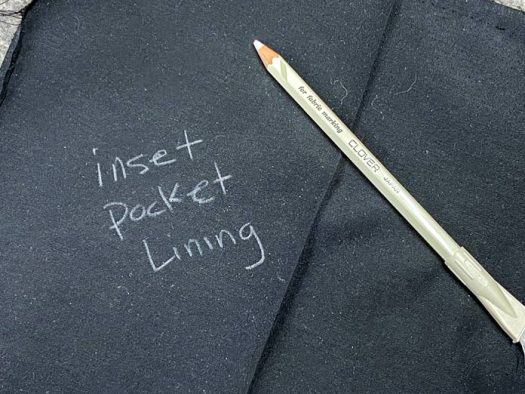 A white fabric pencil sits atop two pieces of black lining fabric. The words “inset pocket lining” have been printed on one of the fabrics.
