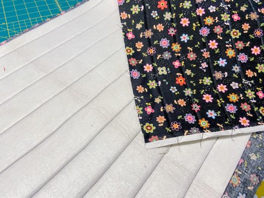 A piece of white stabilizer fused to a black floral fabric is shown so that its parallel quilting lines can be seen.