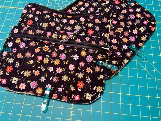 The front and back panels of a black purse, with pockets clipped to them with green clips, sit on top of a green cutting mat. 