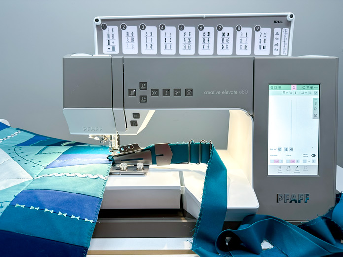 Green Binding loaded in the double-fold quilt binder, on the PFAFF creative elevate 680. The shades of green and blue pieced table center in place, stitching on the green binding