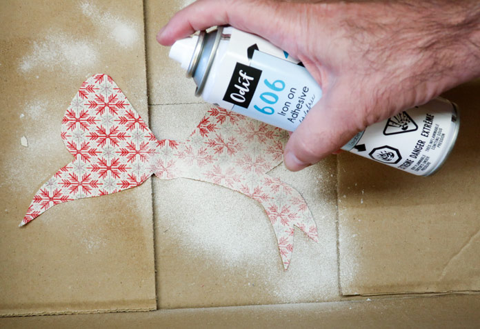 A fabric bow in a cardboard box, with a hand holding a can of spray adhesive positioned above; Odif 606 Spray and Fix No-sew Fusible Adhesive Web, Odif 808 Spray and Fix Temporary Adhesive for Paper Patterns, Odif 404 Spray and Fix Permanent Repositionable Adhesive for Craft Material, Komfort KUT Ruler Cutter, Gütermann 7-pc MCT Sew-all 100m Thread Set – Christmas