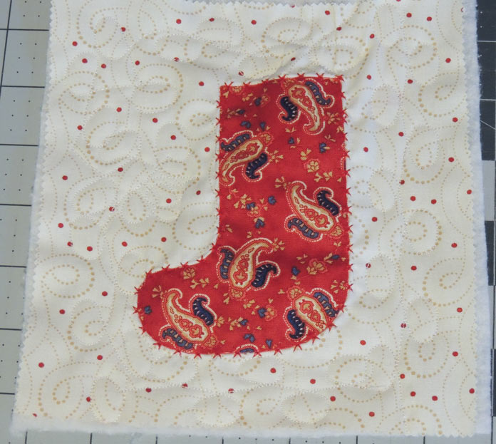A red paisley-printed stocking appliqued on a quilted cream print background fabric