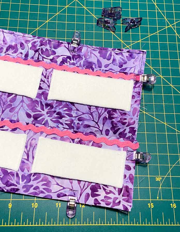 Purple Clever Clips are shown holding together the layers of the needle roll together, with a green cutting mat is in the background. Brother NQ900 sewing machine, UNIQUE quilting Clever Clips, UNIQUE Medium Rick Rack