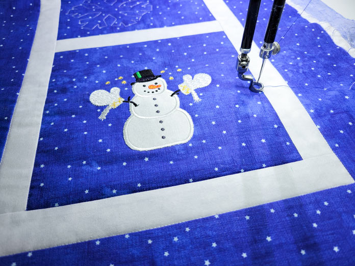 A blue and white table runner with a snowman under the needle of a quilting machine; PFAFF powerquilter 1600