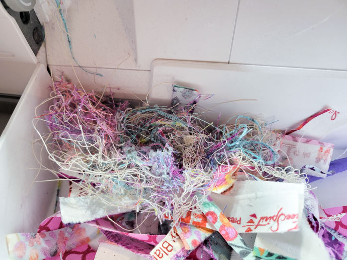 Loose multi-colored threads in a white waste tray on a serger