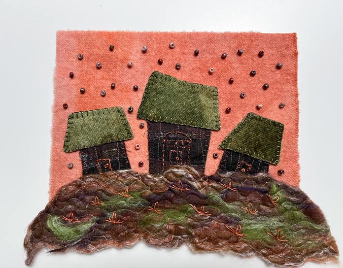 Tiny brown beads are hand-sewn in the orange sky and flower shapes are embroidered on the wool roving foreground; Solvy Water Soluble Stabilizers