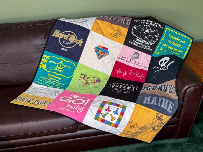 The completed T-shirt quilt is made of 16 squares placed on a couch.