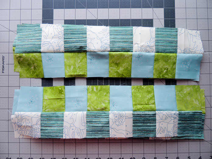 2 piles of strip units with bottom pile turned so matching light green and light blue fabric rows are together with fabrics opposite each other