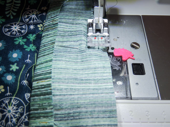 Closeup of fabric layers at the edge of presser foot groove for sewing binding to the back of topper