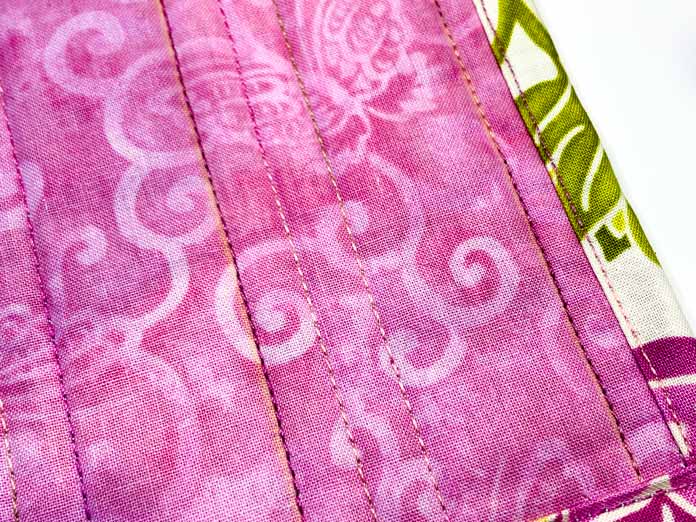 A close-up of the small pink quilt shows the quilting lines and the topstitching that’s been done on the multicolored binding; Sulky Cotton Petites 6 Spool Thread Set - Rosewood Manor Assortment