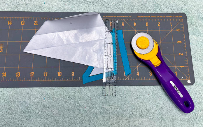 Piece 1 is trimmed with a ¼” seam allowance beyond the freezer paper with a rotary cutter, ruler and cutting mat