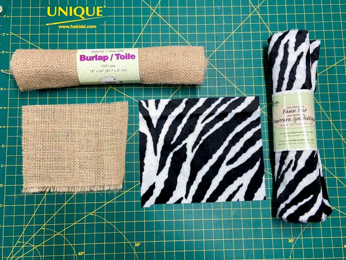 A roll of burlap, a rectangle of burlap, a roll of zebra faux fur, and a rectangle of zebra faux fur are all shown on a green cutting mat. Oliso M2Pro Mini Project Iron, FAIRFIELD Low-Loft Quilt Batting - Crib - 114 x 152cm (45″ x 60″), UNIQUE QUILTING Clever Clips, OLFA CHN-1 - Chenille / Textile Cutter, UNIQUE CREATIV Trim Pack - Black & White, FABRIC CREATIONS Burlap Fabric - Oyster - 45 x 61cm (18″ x 24″), FABRIC CREATIONS Faux Fur Fabric - Zebra - 45 x 76cm (18″ x 30″), UNIQUE SEWING Double Adjust Parachute Buckle - Plastic - 25mm (1″) White, CRAFTING ESSENTIALS Bottle of Buttons - Pink Tones - 75g (2.6oz), UNIQUE SEWING Invisible Magnetic Snaps - Sew-On - 12mm (1⁄2″) - 2 sets, UNIQUE QUILTING Stitch-N-Steam - 157 x 45cm (62″ x 18″), FABRIC CREATIONS Fabric Bundle (5pcs) - Metallic Gold - 45 x 53cm (18in x 21in), Oliso Pro TG1600 Pro Plus Smart Iron, UNIQUE QUILTING Clever Clips Large - 12pcs, sewing tutorial