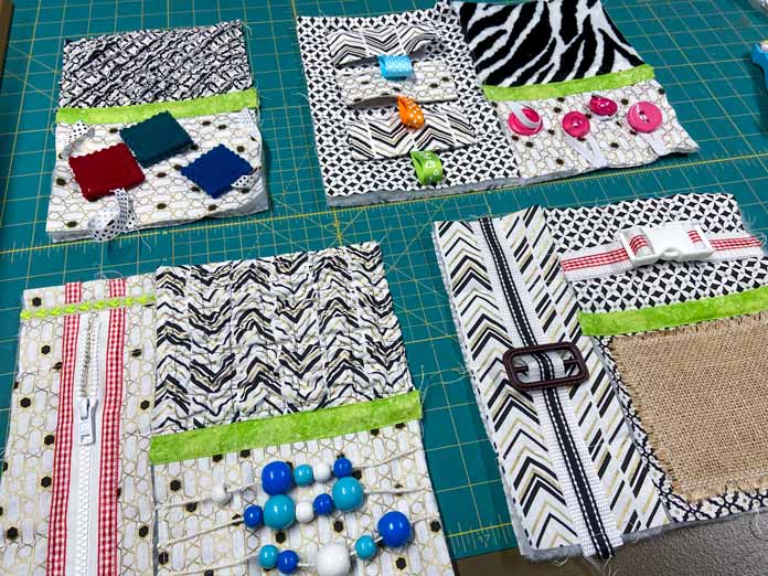 Black, white, and gold textured quilt blocks with brightly colored beads, buttons, and trims for a fidget quilt are shown in groups on a green cutting mat. UNIQUE SEWING Invisible Magnetic Snaps - Sew-On - 12mm (1⁄2″) - 2 sets, COSTUMAKERS General Purpose Closed End Zipper 20cm (8″) - White - 1700, UNIQUE SEWING Double Adjust Parachute Buckle - Plastic - 25mm (1″) – White, UNIQUE QUILTING Clever Clips Small - 12 pcs, CLOVER 7812 Roll & Press, UNIQUE QUILTING Wool Pressing Mat - 18″ x 24″ - Grey, OLISO M2Pro Mini Project Iron with Solemate, CLOVER 240 - Fork Pins - .56mm, CLOVER 464/18 - Bias Tape Maker - 18mm (3⁄4″), Odif 505 Temporary Quilt Basting Adhesive Fabric Spray - 156g, FAIRFIELD Low-Loft® Quilt Batting - Crib - 114 x 152cm (45″ x 60″), free tutorial