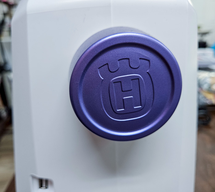 A molded stylized H on a purple button on a white sewing machine; Husqvarna VIKING Designer Quartz 29, mySewnet Machine Embroidery Software