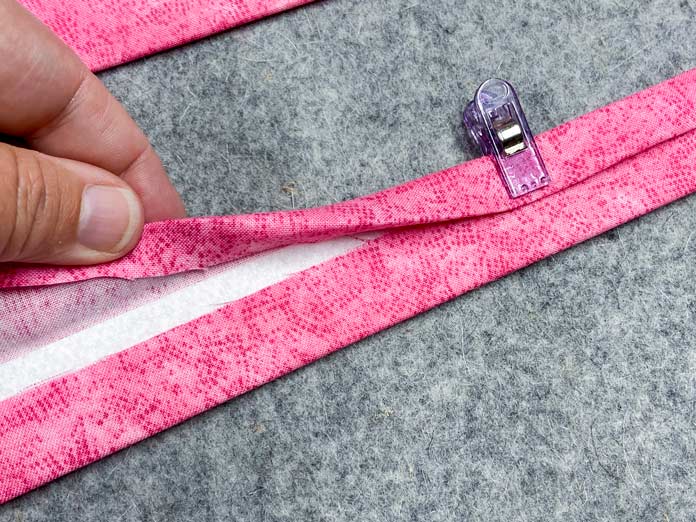 A hand is shown folding under the edge of the fabric strip so that it can be fused to the interfacing.