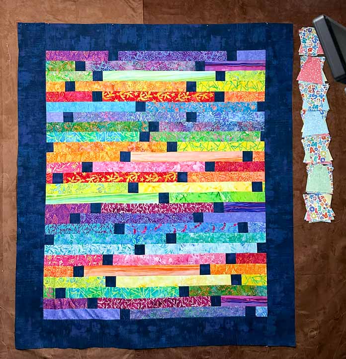 A quilt top pinned to a work board featuring strip piecing with a jelly roll.