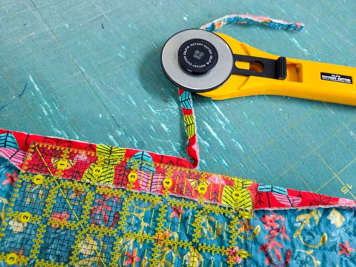 A ruler, a rotary cutter, and red and blue fabric