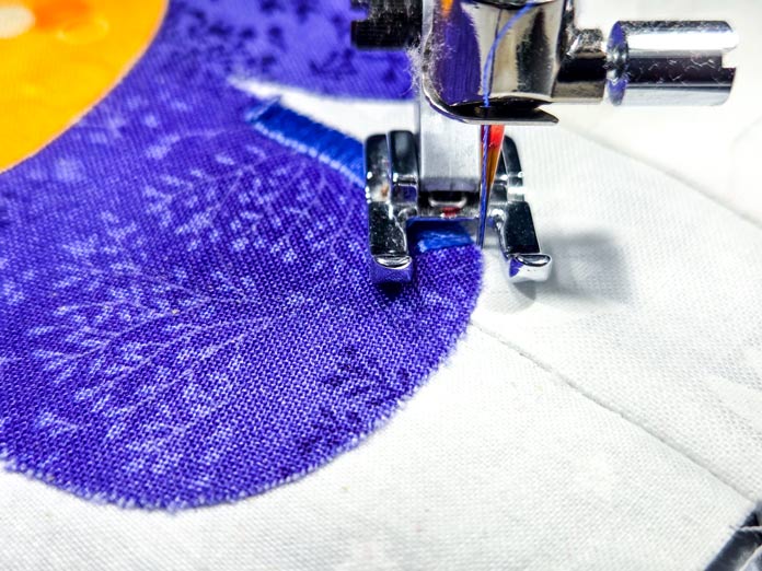 A metal presser foot on purple and white fabrics