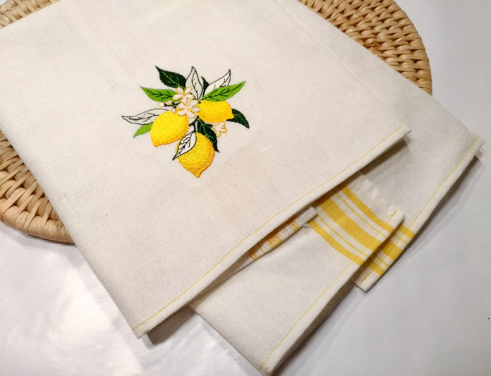 A picture of a folded tea towel, embroidered with a cluster of lemons and leaves; Brother Luminaire XP