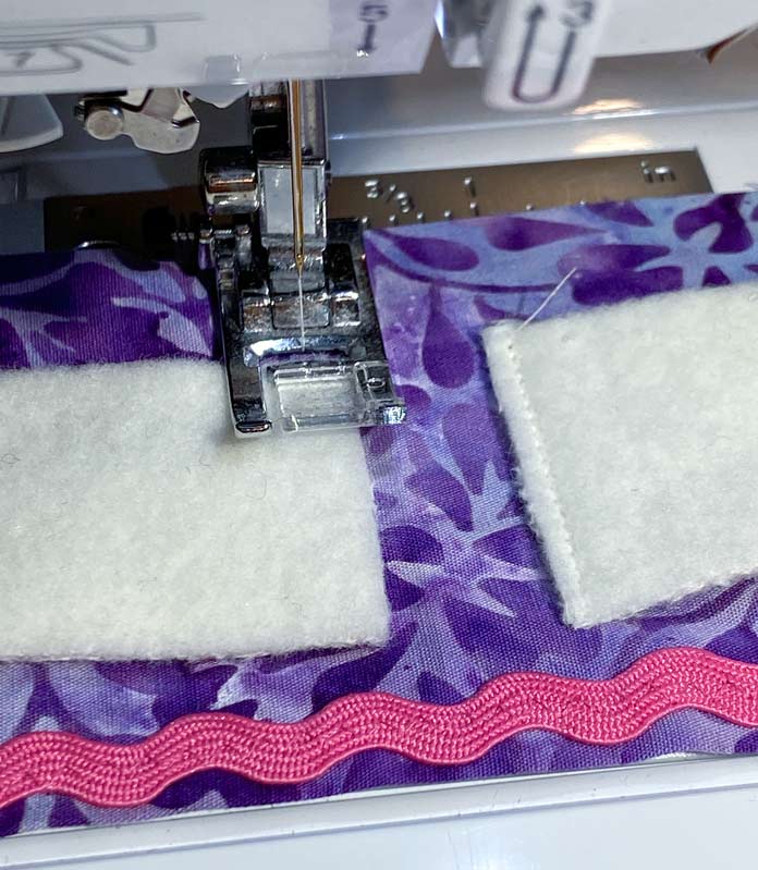 A closeup photo shows the white rectangles of wool being sewn by machine to the purple batik fabric.