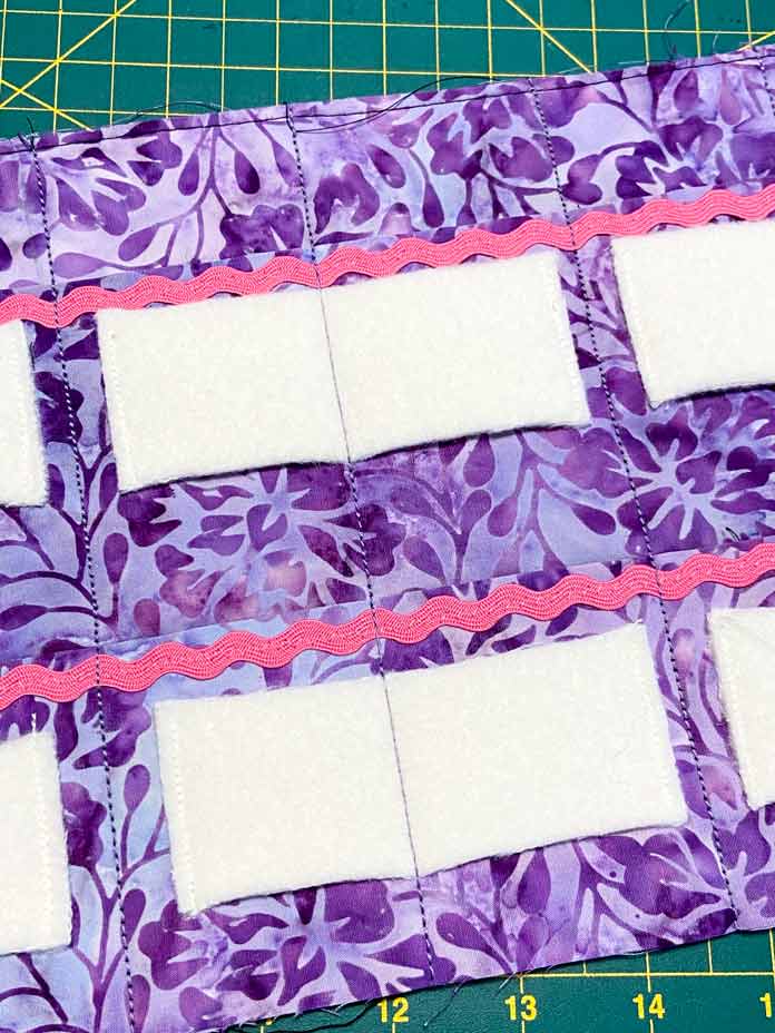 Small pockets are created on purple batik fabric by sewing lines vertically through the center of white wool rectangles stitched to the purple batik, and vertical lines stitched between each white wool rectangle. Brother NQ900 sewing machine, UNIQUE quilting Clever Clips, UNIQUE Medium Rick Rack